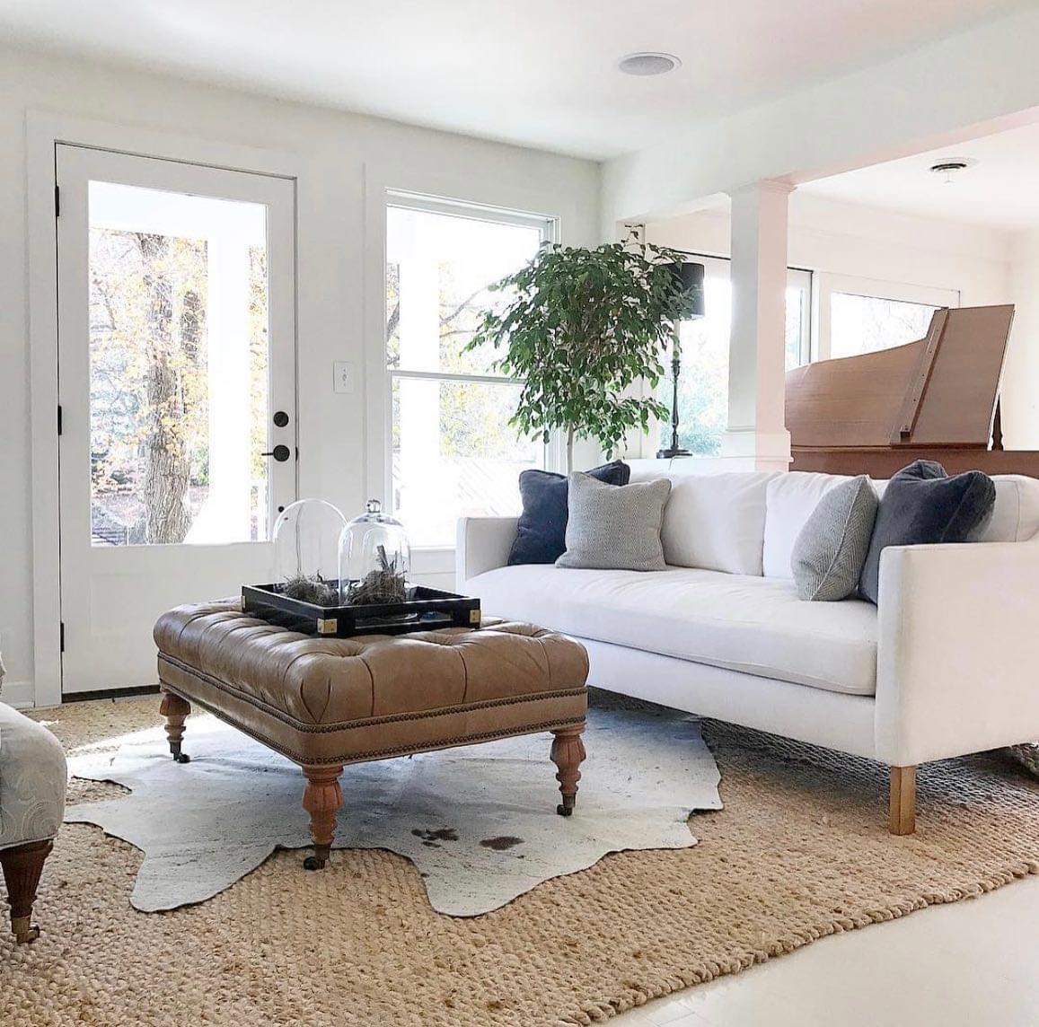 Custom upholstered white sofa with exposed wooden legs and a tufted leather ottoman